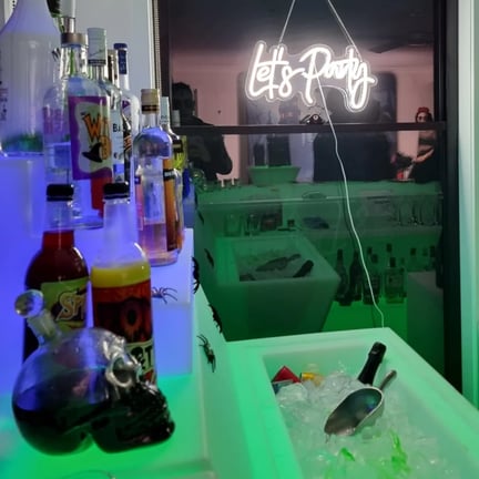 Green glow bar with blue glow drink stand with lets party neon in the background in Redlands.