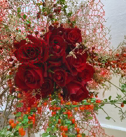 Buchet cu trandafiri roșii, crenguțe decorative și bobițe roșii, pe fundal de plasă roșie.