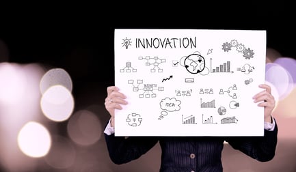 Person in a business suit holding a large whiteboard labeled "Innovation," featuring various hand-drawn diagrams, charts, and