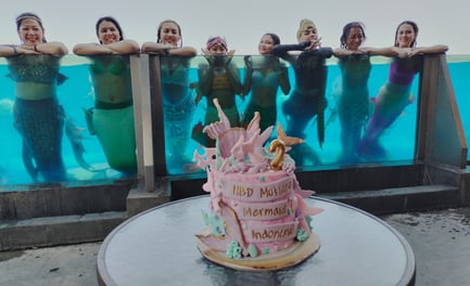 a birthday cake in ocean mermaid theme and the celebrating mermaids in the background, swimming in a