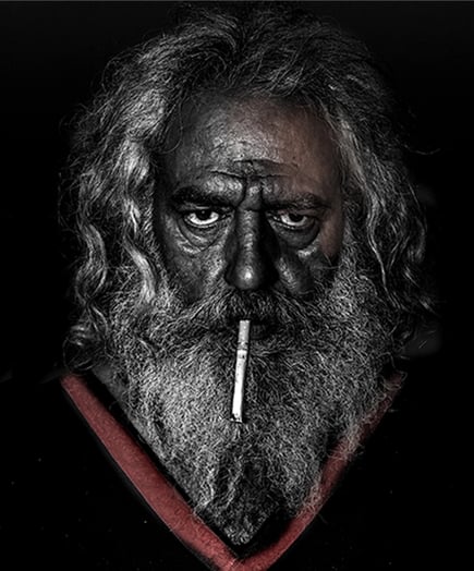 Portrait of an older man with a weathered face and intense gaze, cigarette held between his lips.