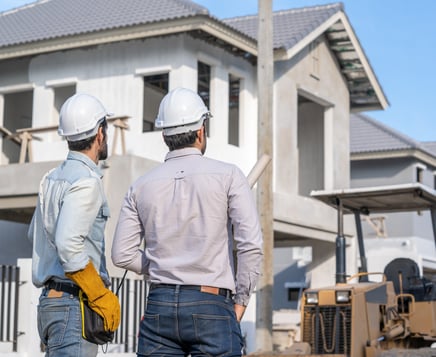 two men in hard hats standing in front of a house