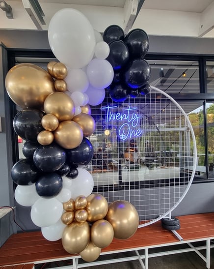 White circle mesh backdrop with blue Twenty One neon sign and a gold, black and white balloon garland, Redlands