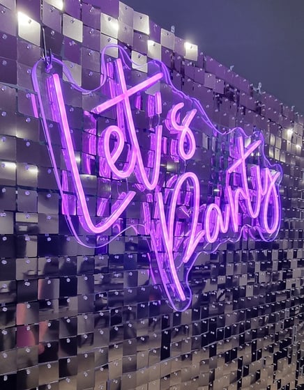 Glowing pink Let's Party neon sign on a silver shimmer wall for an event in Brisbane.