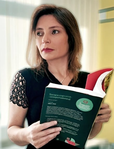 Psicóloga Dayane Machado Terapia Cognitiva Comportamental tcc olhando para o lado pensativa segurando um livro