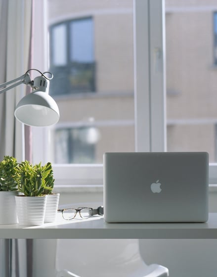 Modern home office desk with a laptop, desk lamp, green plants, and eyeglasses