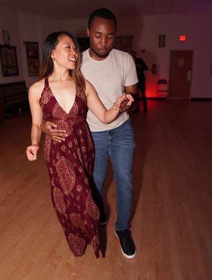 A couple dancing together in a social dance setting, with one partner wearing a flowing maroon dress