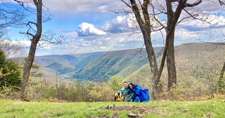 a couple with dog hiking and sitting on a mountain top peak