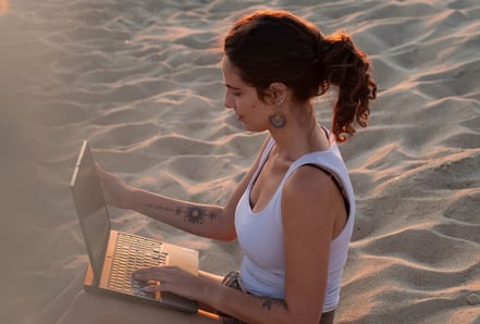 a woman sitting on a beach with a laptop