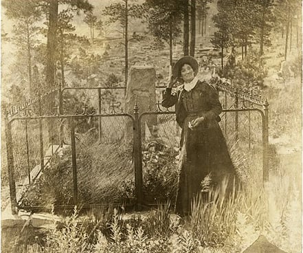 Calamity Jane standing in front of Wild Bill Hickok's grave.