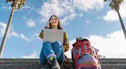 a woman sitting on stairs with a laptop and a backpack