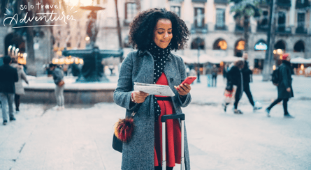 a woman in a coat and scarf standing in a city
