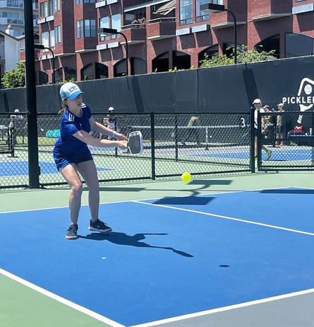 Woman hitting a backhand shot during outdoor pickleball play at a Smart Dinker session.