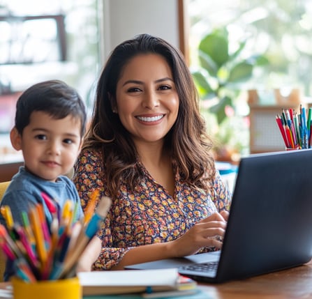 Mamá emprendedora sonriente con su hijo junto a la laptop, representa emprendimiento digital desde casa en familia..