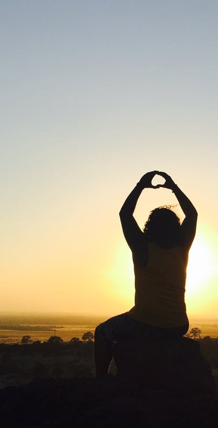 Man sitting down watching the sunset with his hands in the air