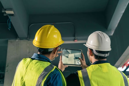 two men in safety vests and safety vests are looking at a tablet computer