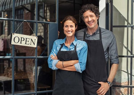 A husband and wife standing in front of their business that they own together