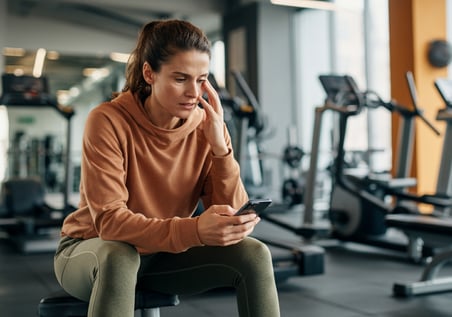 vrouw die op een bankje zit in de sportschool met een gsm in haar hand