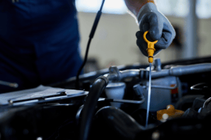 Close-up of an auto mechanic checking engine oil with a dipstick inside a vehicle repair shop.