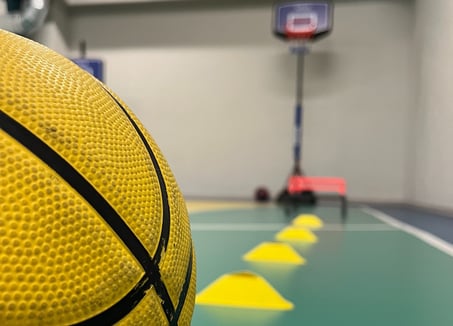 Primo piano di un pallone da basket giallo in un'area multisport della palestra Move 2 Grow a Milano, con coni e canestro sul