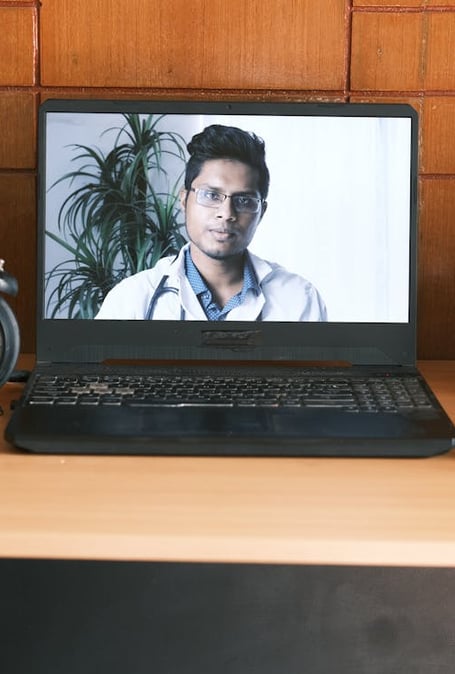 a laptop computer screen showing a doctor's face on a desk