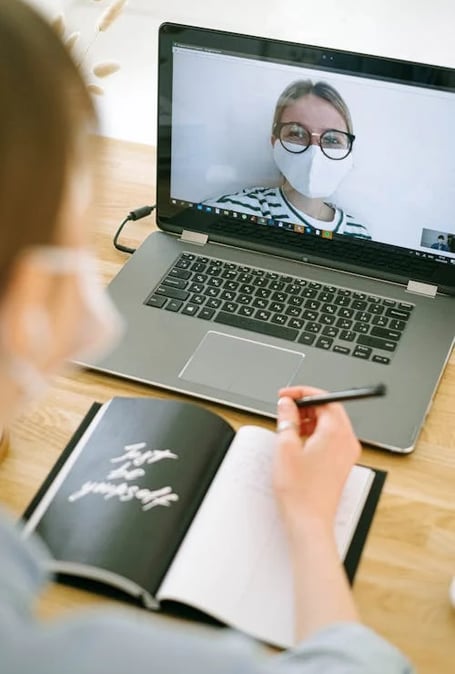 a woman in a mask mask and glasses is looking at a laptop computer screen