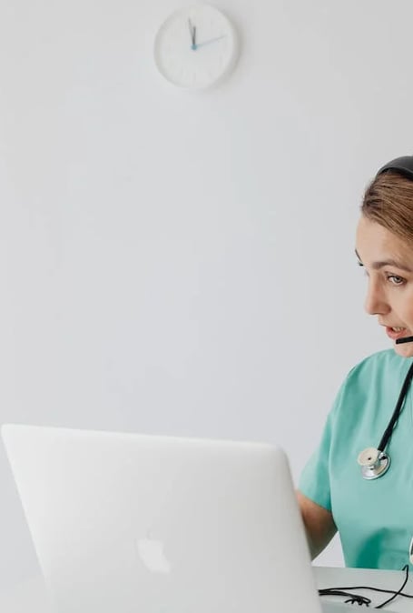 a nurse in a green scrub suit and a stethoscope on a laptop