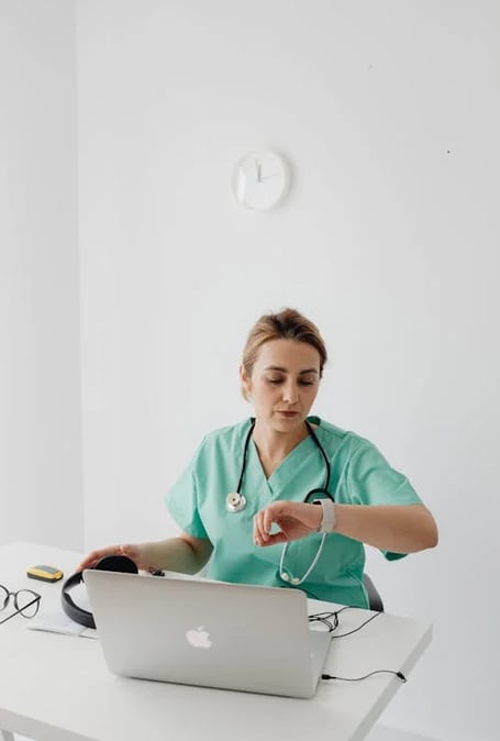 a nurse in scrubs and a stethoscope on a laptop