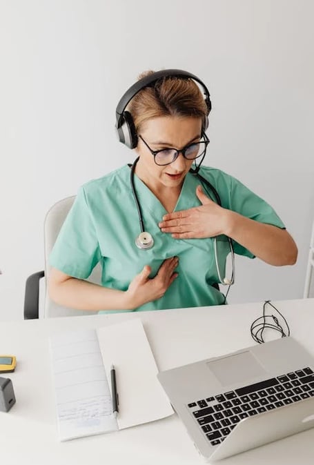 a nurse in a green scrubsuit is holding her hands on her chest