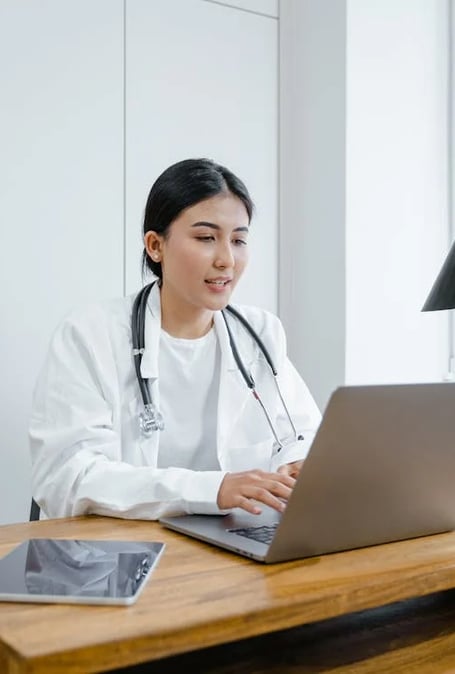 a woman in a white lab coat and a stethoscope on a laptop