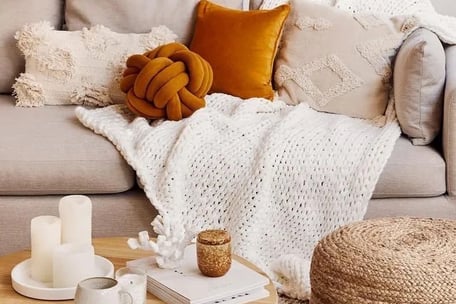 Couverture et coussins dans les tons beige et orange posés sur un canapé