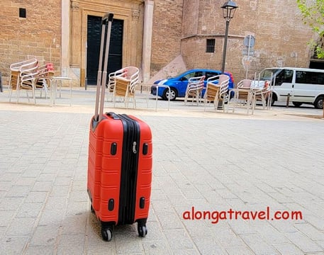 A small red carry-on standing in the middle of a square shows an ease of moving when packed light 