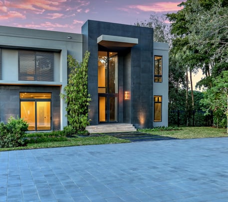 a luxury home lit up at night with a large driveway and a vibrantly colored sky