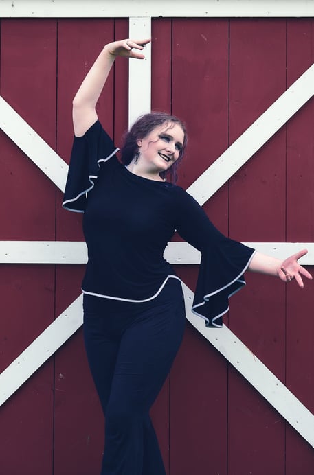 a woman in a black top and pants dancing in front of a barn