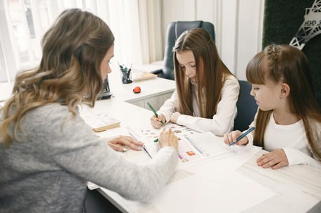 "Home tutor teaching two students, providing personalized instruction in a comfortable setting."