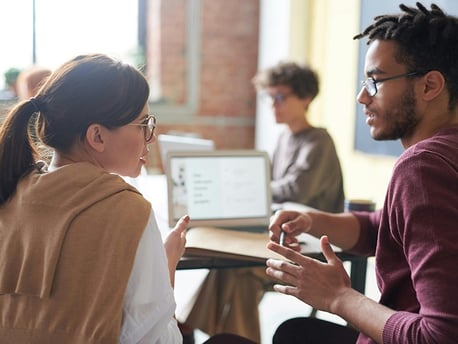 homem e mulher conversando em sala de aula com um notebook ao fundo