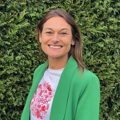 Lady stood before a hedge in a green coat smiling