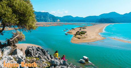 a couple of people standing on a cliff overlooking İztuzu Beach