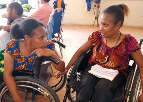 two women in wheelchairs conversing with each other.