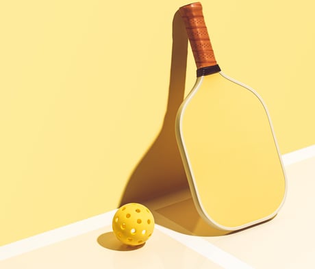 Minimalist yellow pickleball paddle and ball on a bright court, representing Smart Dinker’s sport