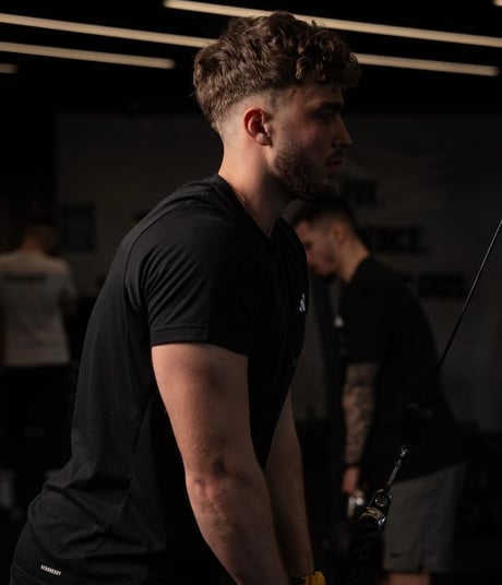 Barbat la sala, executa extensii pentru triceps la scripete, imbracat in negru.