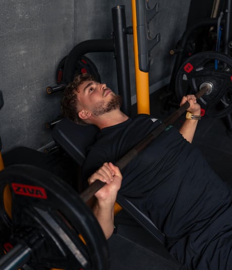 Barbat face impins la piept cu bara pe banca inclinata, echipat in negru.