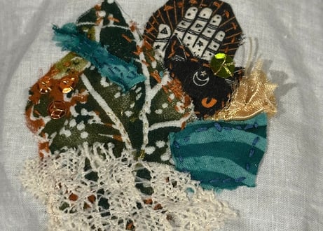 fabric collage with sequins in shades of green, teal, rust, black and cream; cat face and lace used