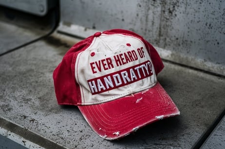 a red and white cap with the inscription “ever heard of handratty?”