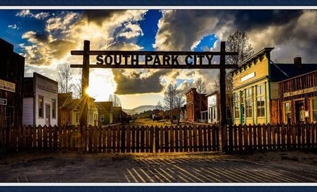 Wooden gate marked "South Park City" leading into a historic western town replica at sunset.
