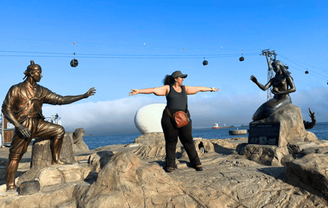 Trisha standing at Songdo Bay in Busan between the statue of the Mermaid and the villager