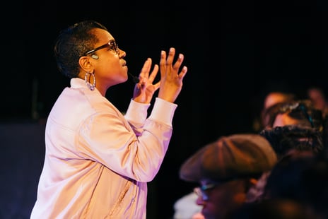 a Black woman in a pink jacket and glasses among audience