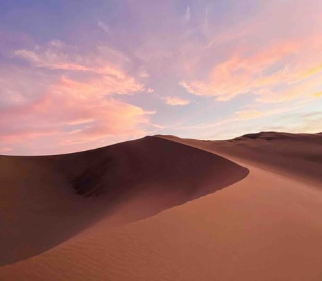 A beautiful sunset over the sand dunes of Huacachina desert in Peru, with bright orange and pink colors filling the sky.