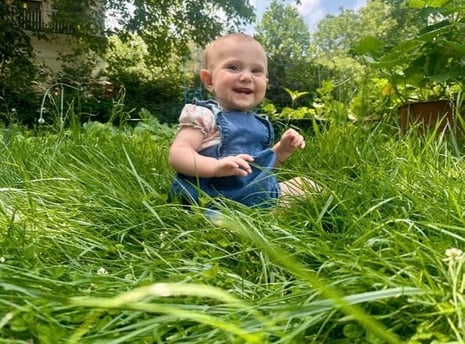 A happy baby girl sitting in the tall grace smiling at the camera representing mother baby bond