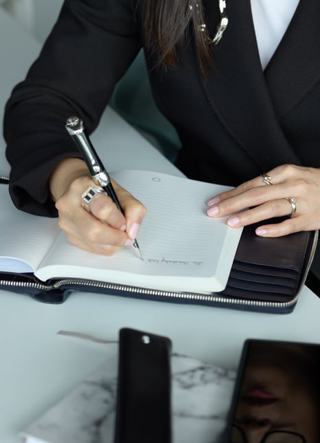 Ka Ming Zwingenberger in a suit writing on a notebook with a writing instrument.